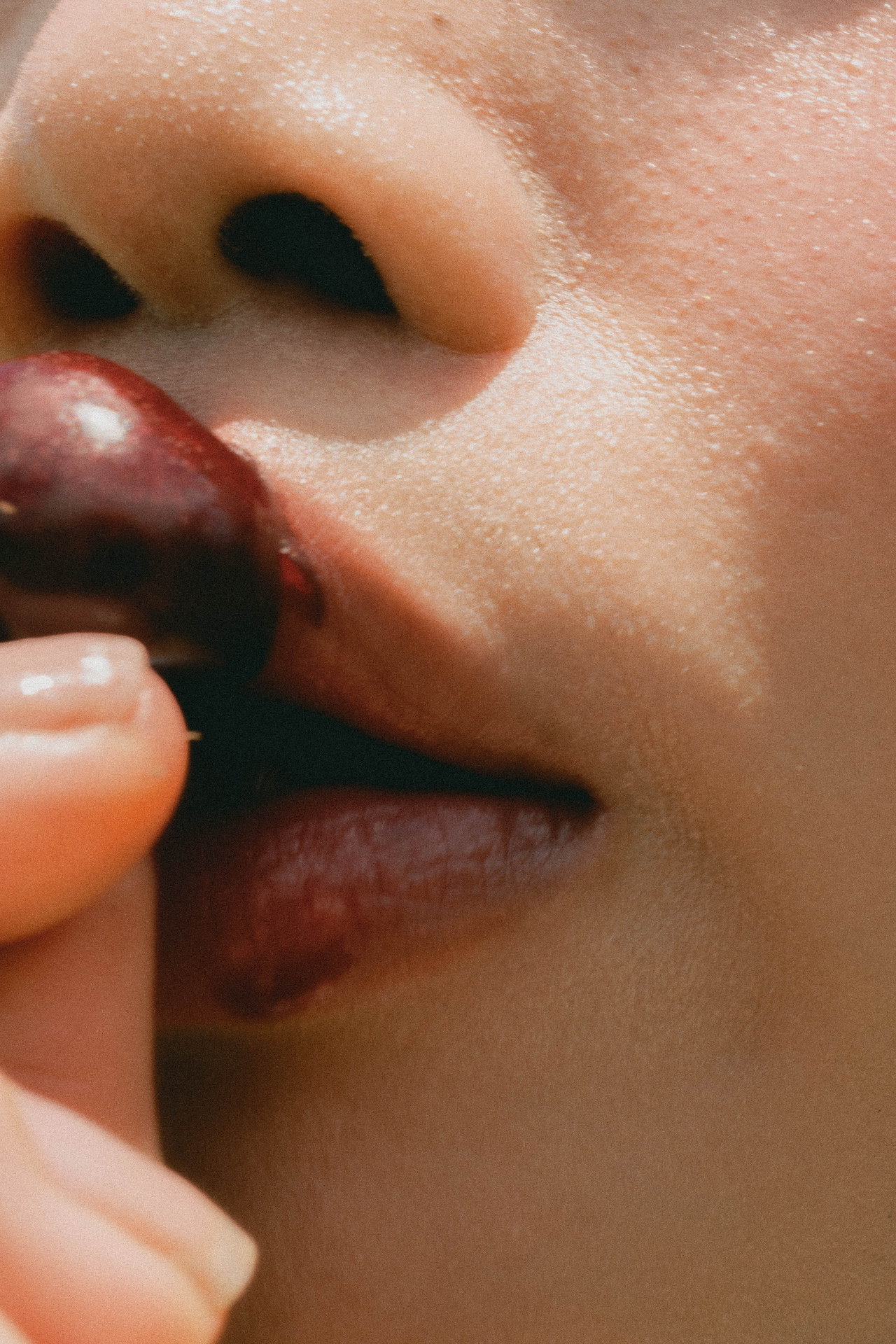 Close portrait of a woman tasting a dark red cherry in warm daylight