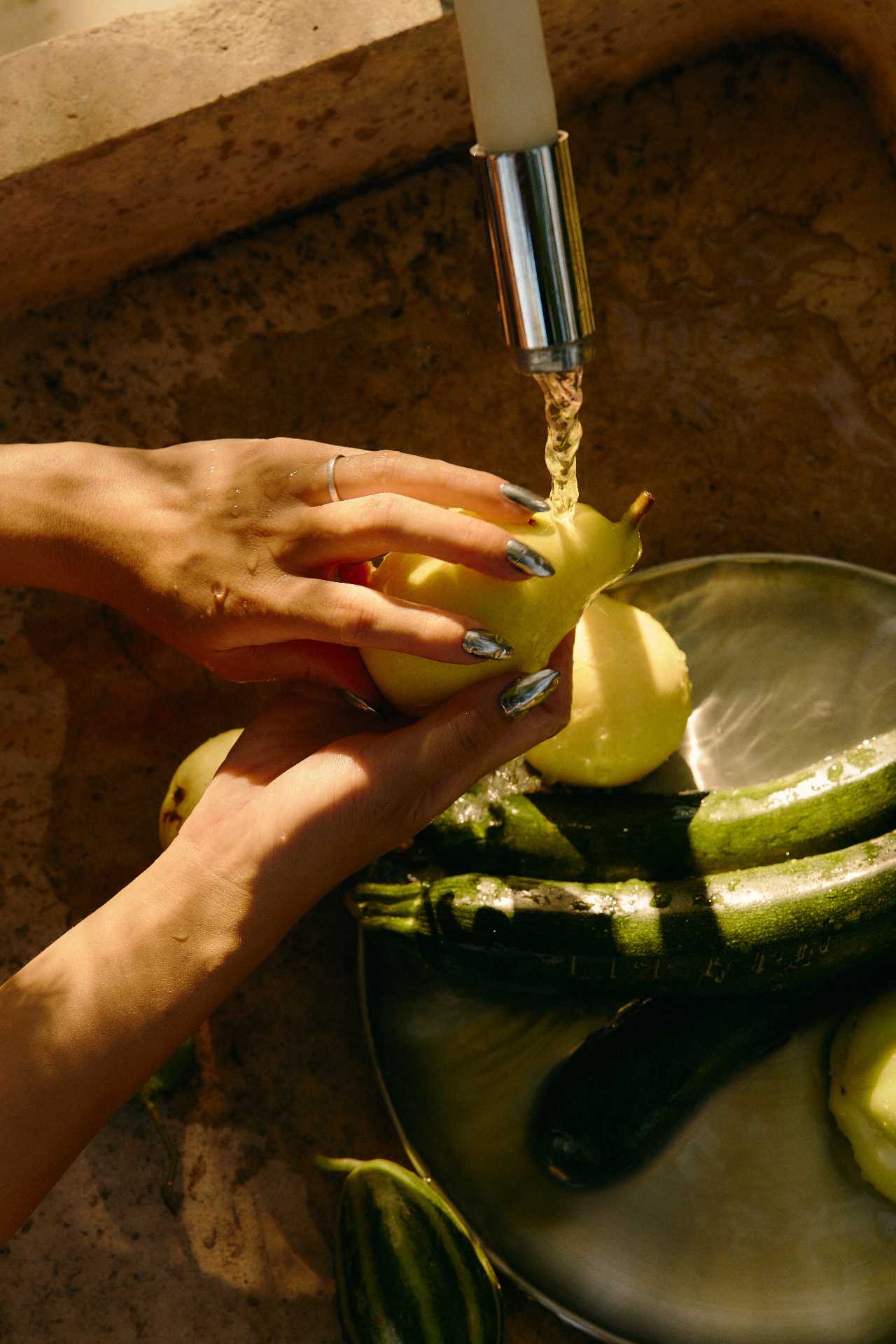 Hands rinsing fresh squash and zucchini in a sunlit kitchen sink